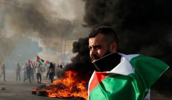 A man draped in a Palestinian flag looks on near a tire fire during clashes with Israeli forces in the West Bank on May 29.