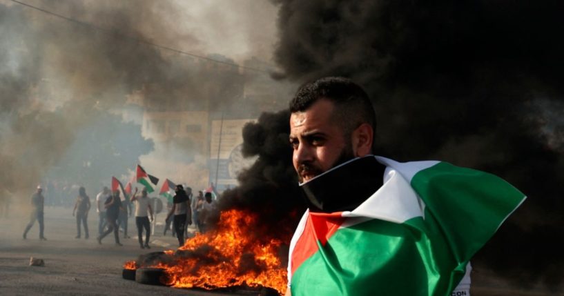 A man draped in a Palestinian flag looks on near a tire fire during clashes with Israeli forces in the West Bank on May 29.