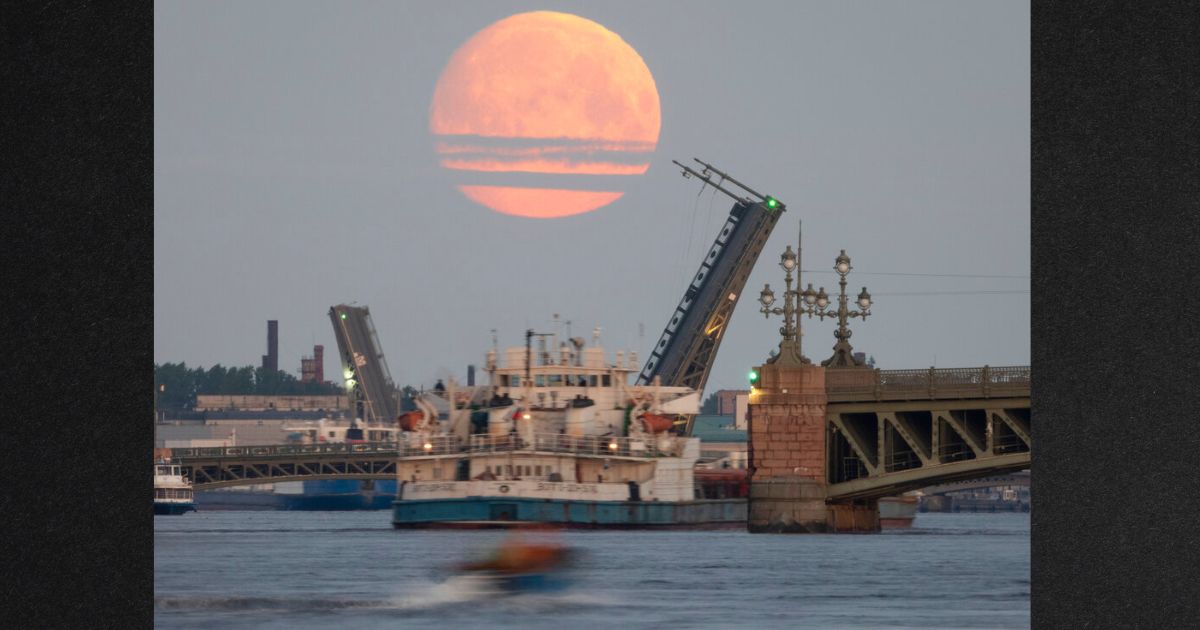 A cargo ship travels past as drawbridges rise above the Neva River, with the moon in the sky, in St. Petersburg, Russia, in this file photo from May 2021. The U.S. has been quietly urging U.S. companies to buy and carry Russian fertilizer and other products, but the companies are reluctant, fearing the prospect of costly sanctions.