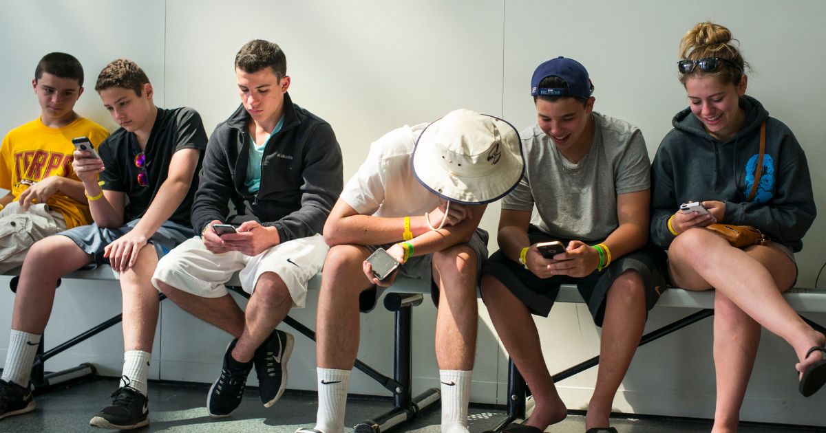 A group of teenagers look at their Apple iPhones while sitting in the Rock and Roll Hall of Fame in Cleveland, Ohio, on July 3, 2015.