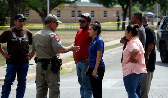 A police officer talks to civilians outside Robb Elementary School in Uvalde, Texas, after the May 24 school shooting that left 19 children and two adults dead. (A police officer talks to civilians outside Robb Elementary School in Uvalde, Texas, after the May 24 school shooting that left 19 children and two adults dead.