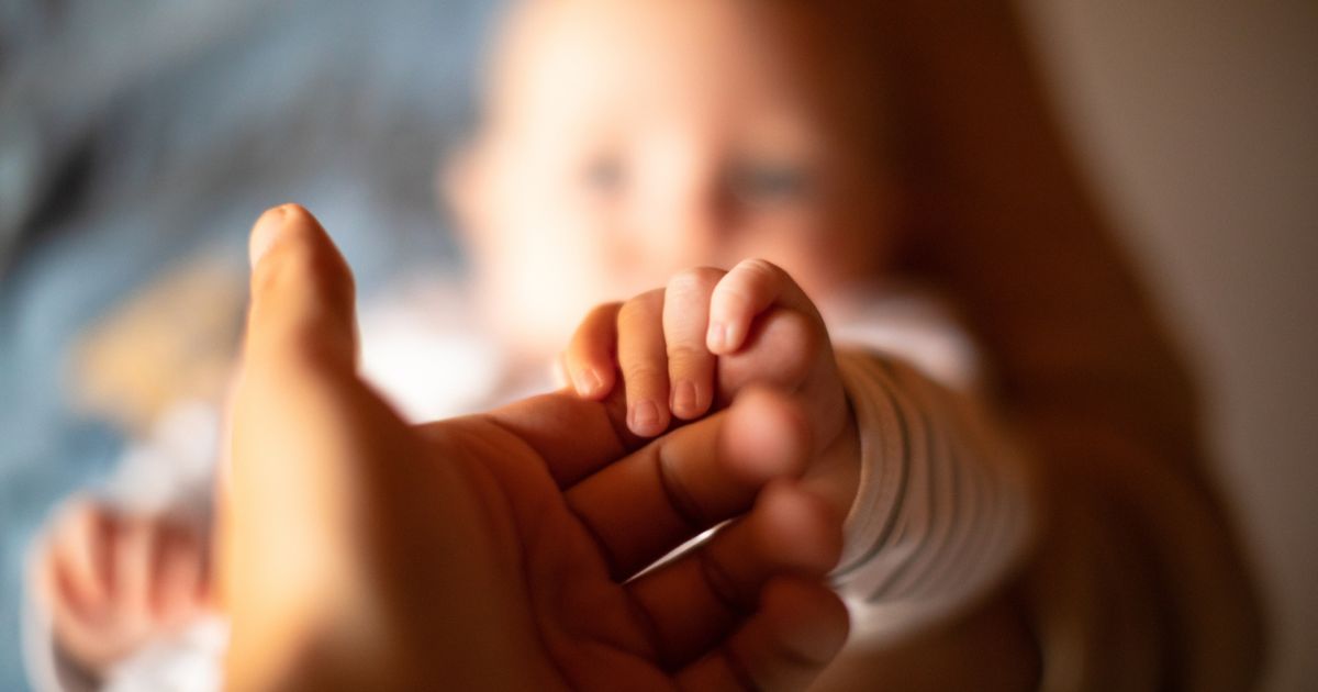 A baby holds a man's hand in the above stock image.