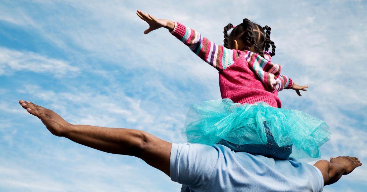 A father carries his daughter on his shoulders in this stock image.