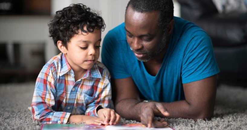 A father reads to his son in the above stock image.