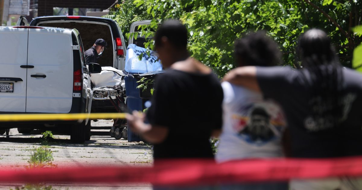 People watch as the body of a shooting victim is loaded into a van on June 15, 2021, in the Englewood neighborhood of Chicago.