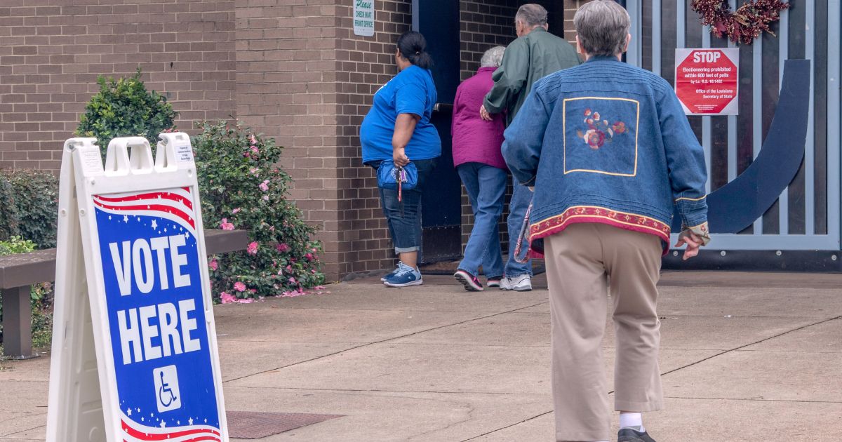 Four voters enter a polling place near a sign that read 'vote here.'