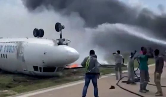 Rescue crews attempt to put out a fire on an upside-down plane surrounded by smoke.