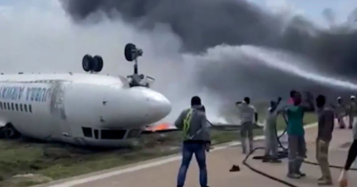 Rescue crews attempt to put out a fire on an upside-down plane surrounded by smoke.