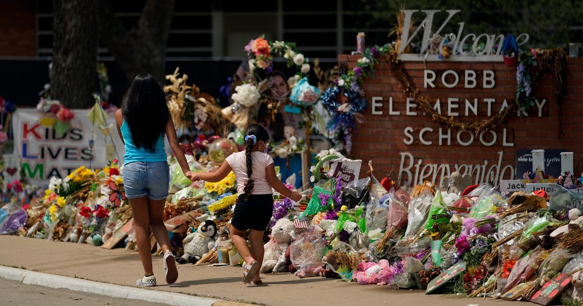Visitors walk past a makeshift memorial outside of Robb Elementary School in Uvalde, Texas, on July 12 that was made to honor those killed in the school's recent shooting.