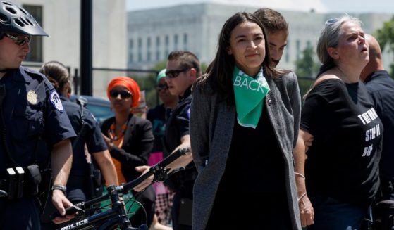 Rep. Alexandria Ocasio-Cortez grins while holding a pose that makes her appear to be handcuffed after being arrested at a protest outside the Supreme Court on Tuesday.