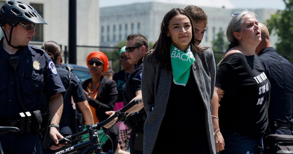 Rep. Alexandria Ocasio-Cortez grins while holding a pose that makes her appear to be handcuffed after being arrested at a protest outside the Supreme Court on Tuesday.