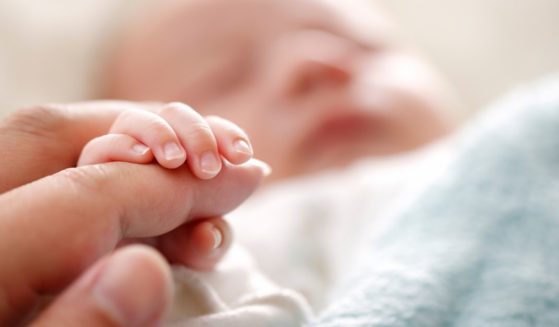 A baby holds its mother's finger in this stock image.