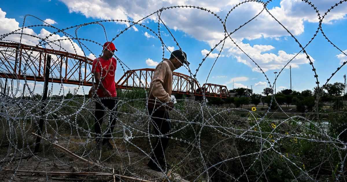 Migrants who illegally crossed the Rio Grande walk along concertina wire in Eagle Pass, Texas, on June 30.