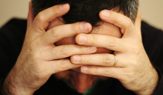 A man, presumably fed up with President Joe Biden, holds his head in his hands in the above stock image.