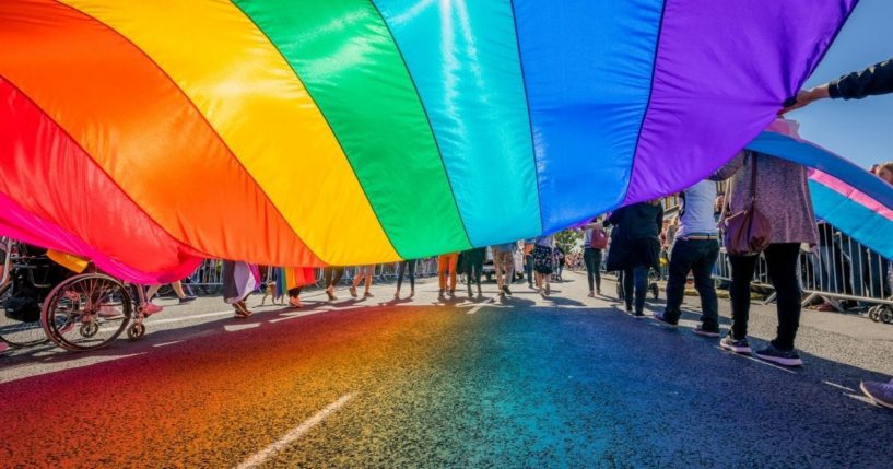 People marching on a street with a large rainbow-colored flag.