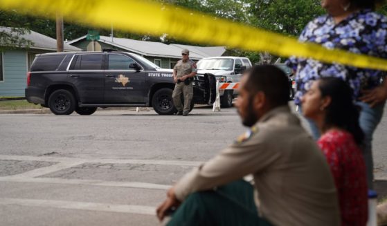 Individuals sit on the curb outside of Robb Elementary School as State troopers guard the area in Uvalde, Texas, on May 24.