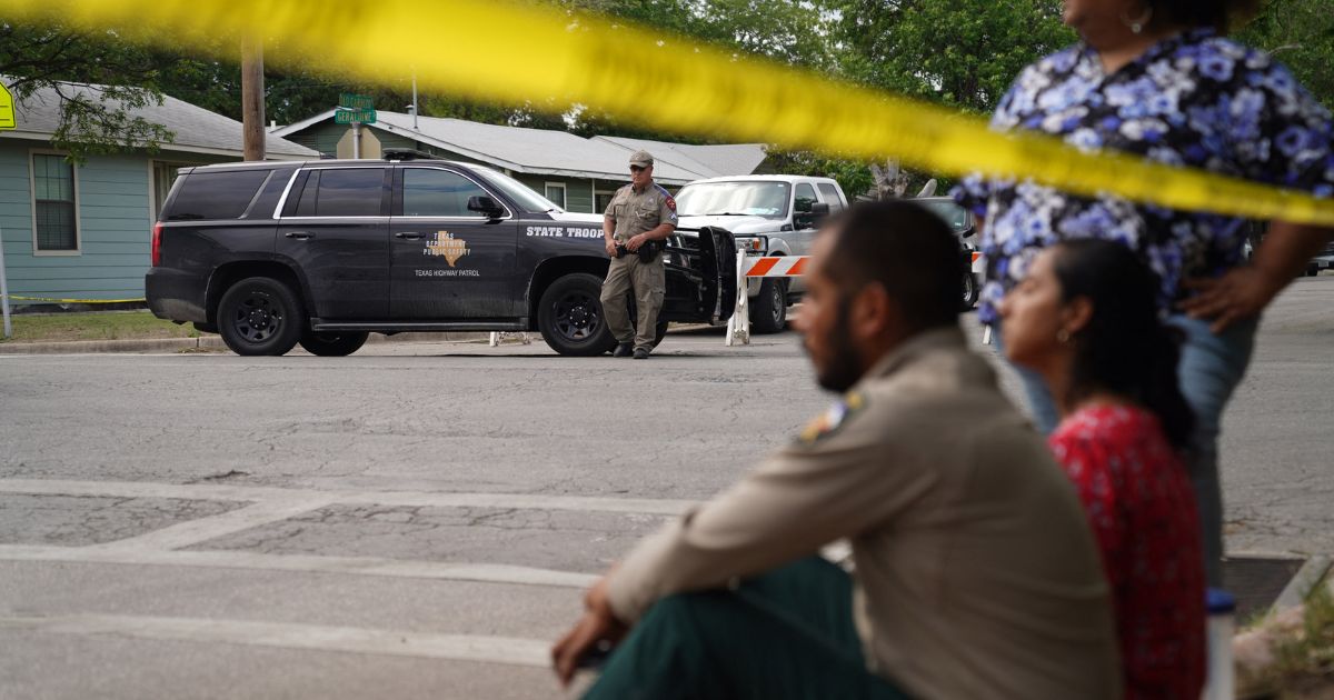 Individuals sit on the curb outside of Robb Elementary School as State troopers guard the area in Uvalde, Texas, on May 24.