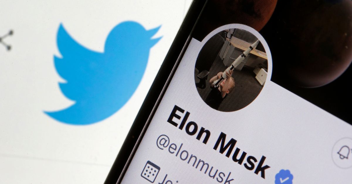 In this photo illustration, Elon Musk’s Twitter account is displayed on the screen of an iPhone in front of a Twitter logo.