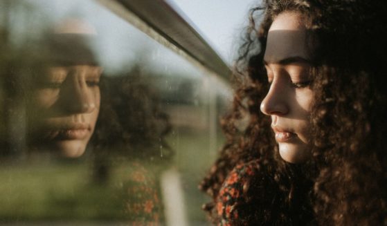 A young woman looks out a window in this stock image.