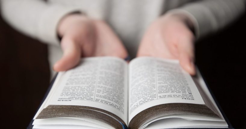 A person holds an open Bible in the above stock image.