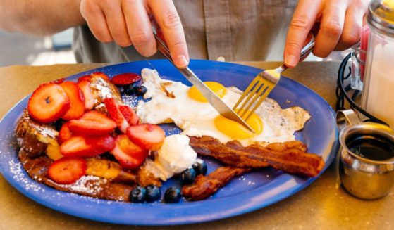 A man eats breakfast with french toast, eggs, bacon and fresh fruit.
