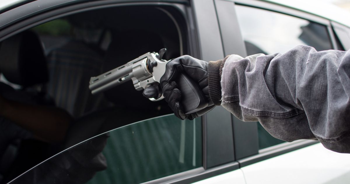 In this concept photo, a man attempts to rob another of his car by using a gun and forcing open the car door.