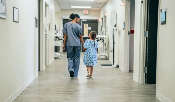 A nurse walks a young girl down a hospital corridor.