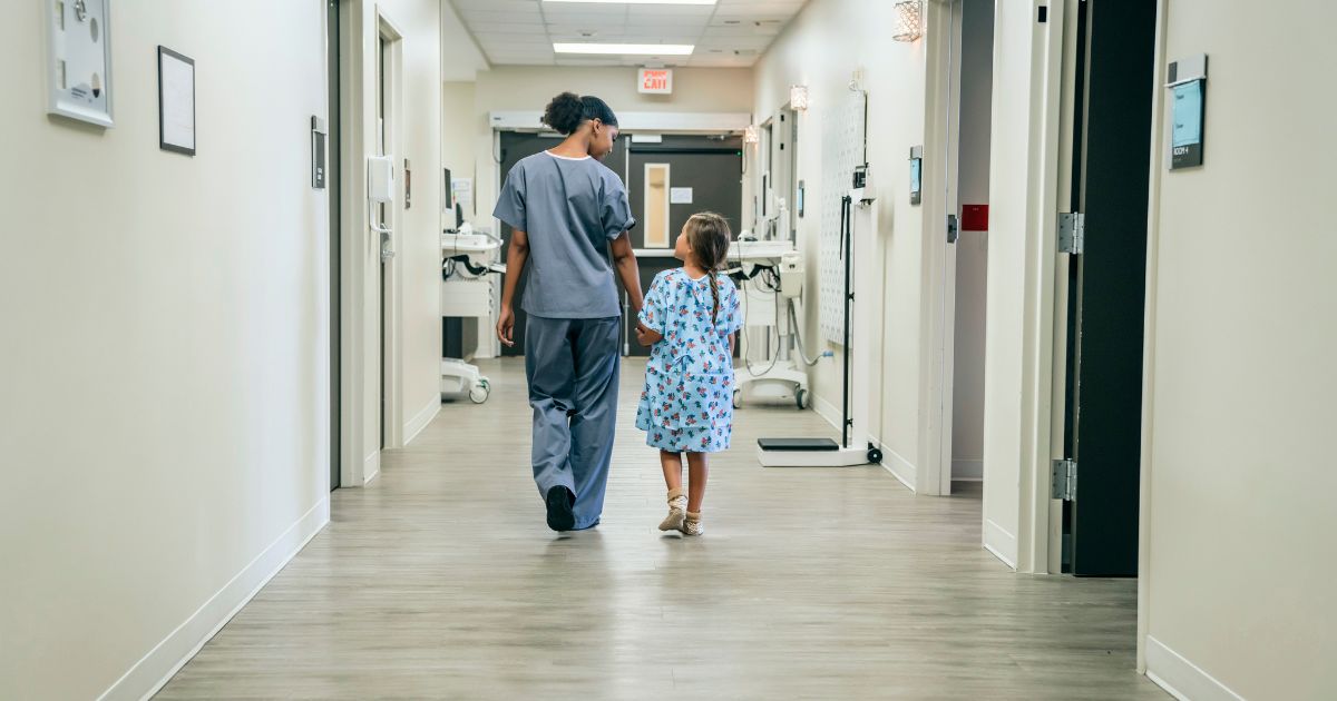 A nurse walks a young girl down a hospital corridor.