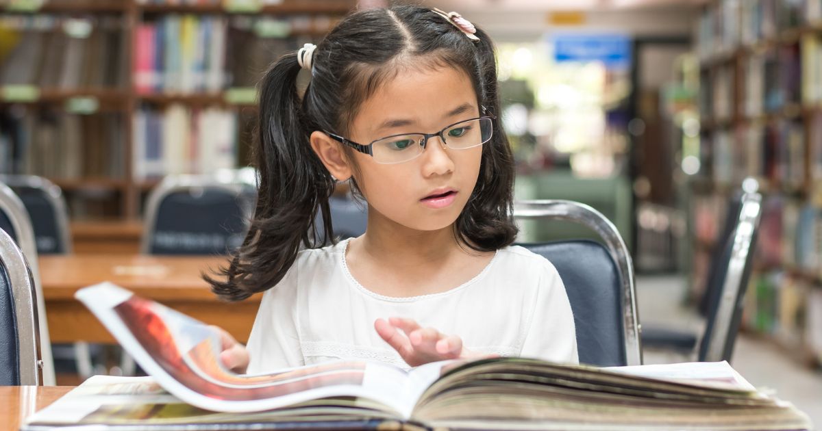 A young girl looks at a book in the school library.