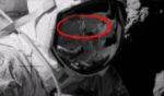 The image appears to show a person reflected in the astronaut's helmet who may or may not be wearing a space suit.