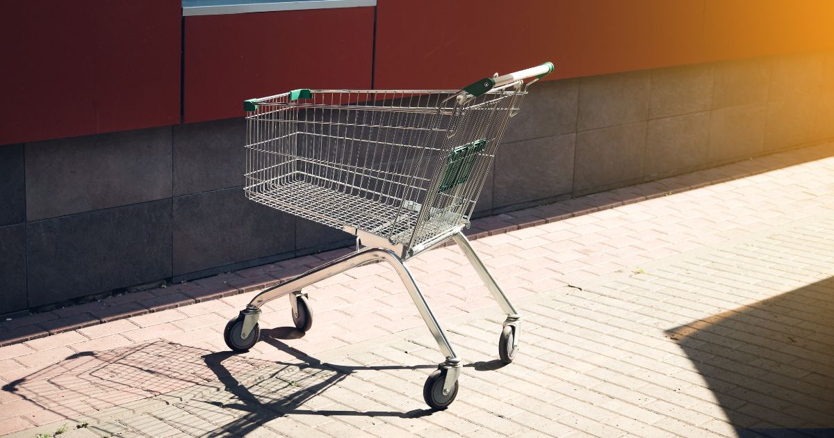 A shopping cart for groceries and other goods is parked near a store.