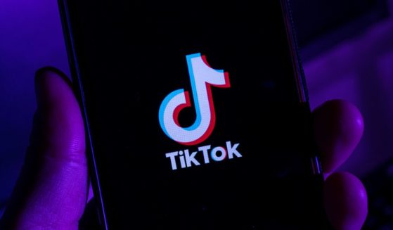 A man holds a cellphone with the TikTok app displayed.