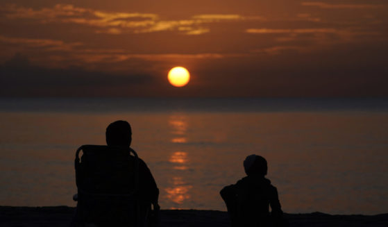 A pair of beach goers watch the sun rise over the Atlantic Ocean
