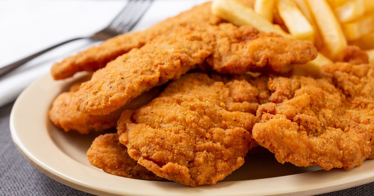 A plate of chicken tenders sits on a table in this stock image.
