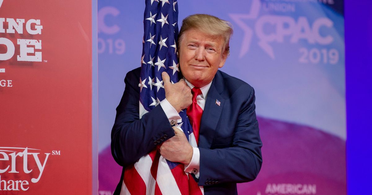 President Donald Trump hugs the U.S. flag during CPAC 2019 on March 2, 2019, in National Harbor, Maryland.