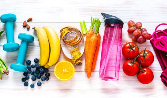 A photographer captures an exercising and healthy eating concept with a rainbow colored overhead view of workout equipment, fruits and vegetables.