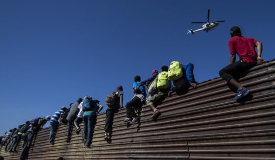 A group of illegal immigrant from Central America climb over a metal barrier on the U.S.-Mexico border near Tijuana, Mexico, on Nov. 25, 2018.