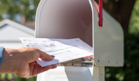 A stock photo shows someone reaching into a mailbox for applications to vote by mail.
