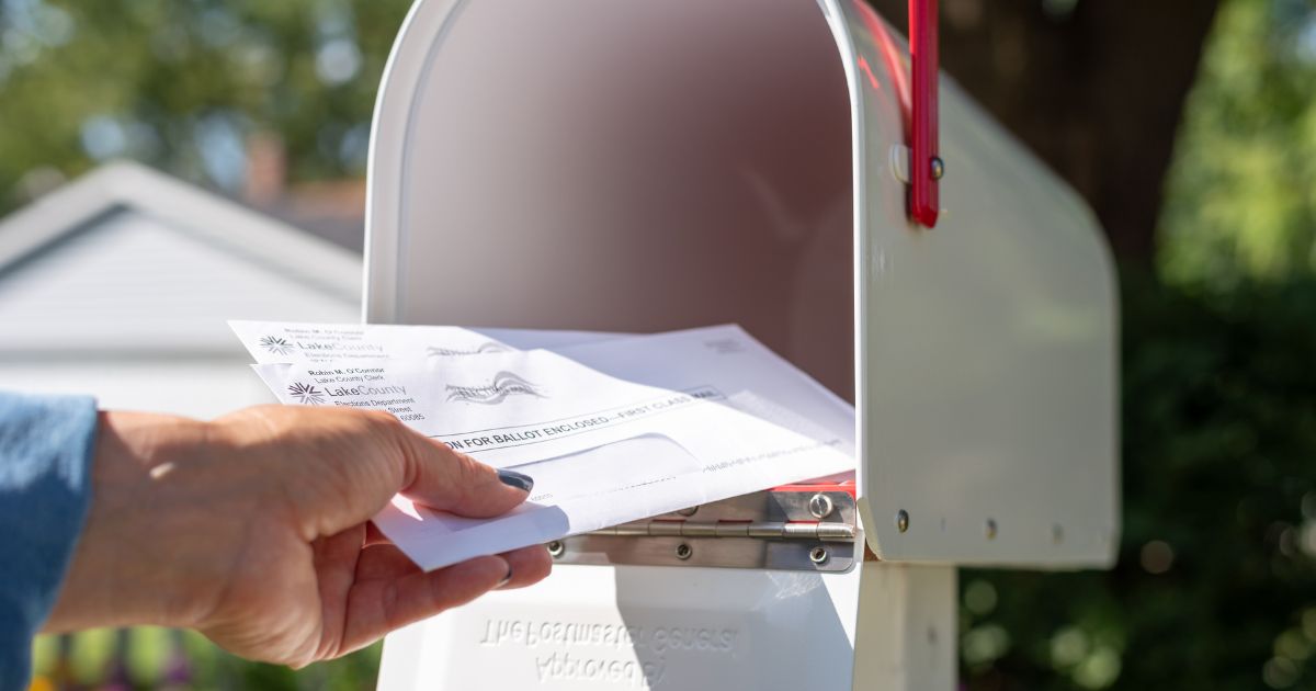 A stock photo shows someone reaching into a mailbox for applications to vote by mail.