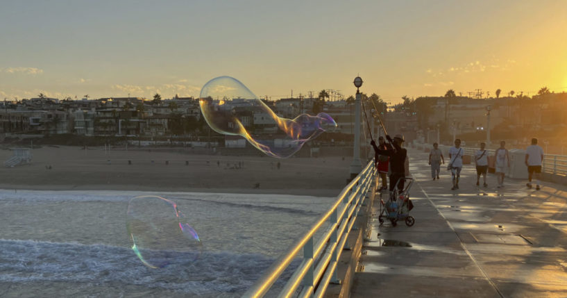 a man creating giant soap suds bubbles at dawn on a California pier