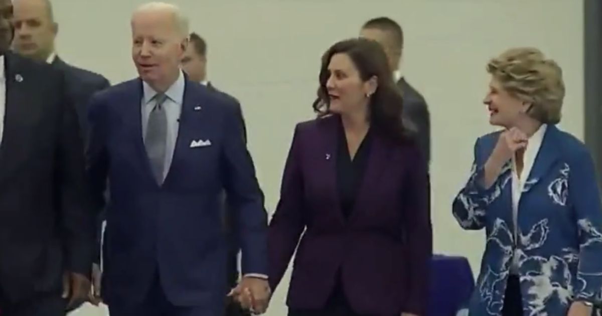 President Joe Biden, left, holds hands with Michigan's Gov. Gretchen Whitmer, right, at the Detroit Auto Show.