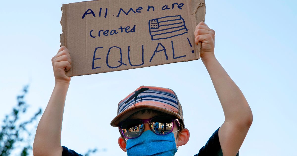 a boy holding a sign saying "All men are created equal"