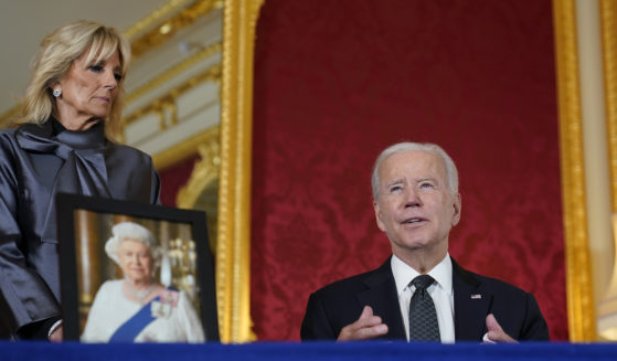 President Joe Biden, right, sits down to sign an official condolence book for Queen Elizabeth II at Lancaster House in London on Sunday.