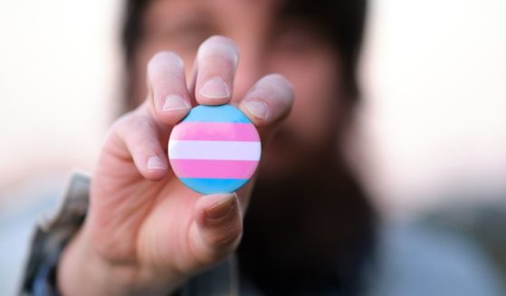The above stock image is of a man holding a pin with transgender colors.