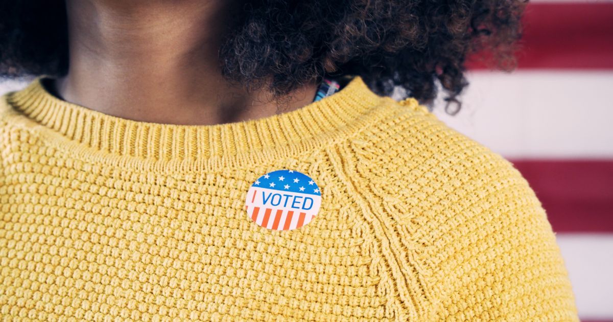 A woman wears an "I Voted" sticker in this stock image.