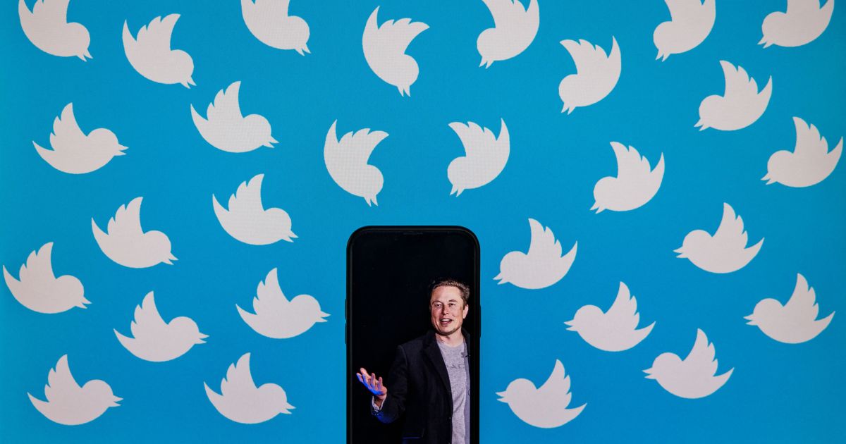 This illustration image shows a cellphone displaying a photo of Elon Musk placed on a computer monitor displaying Twitter logos.