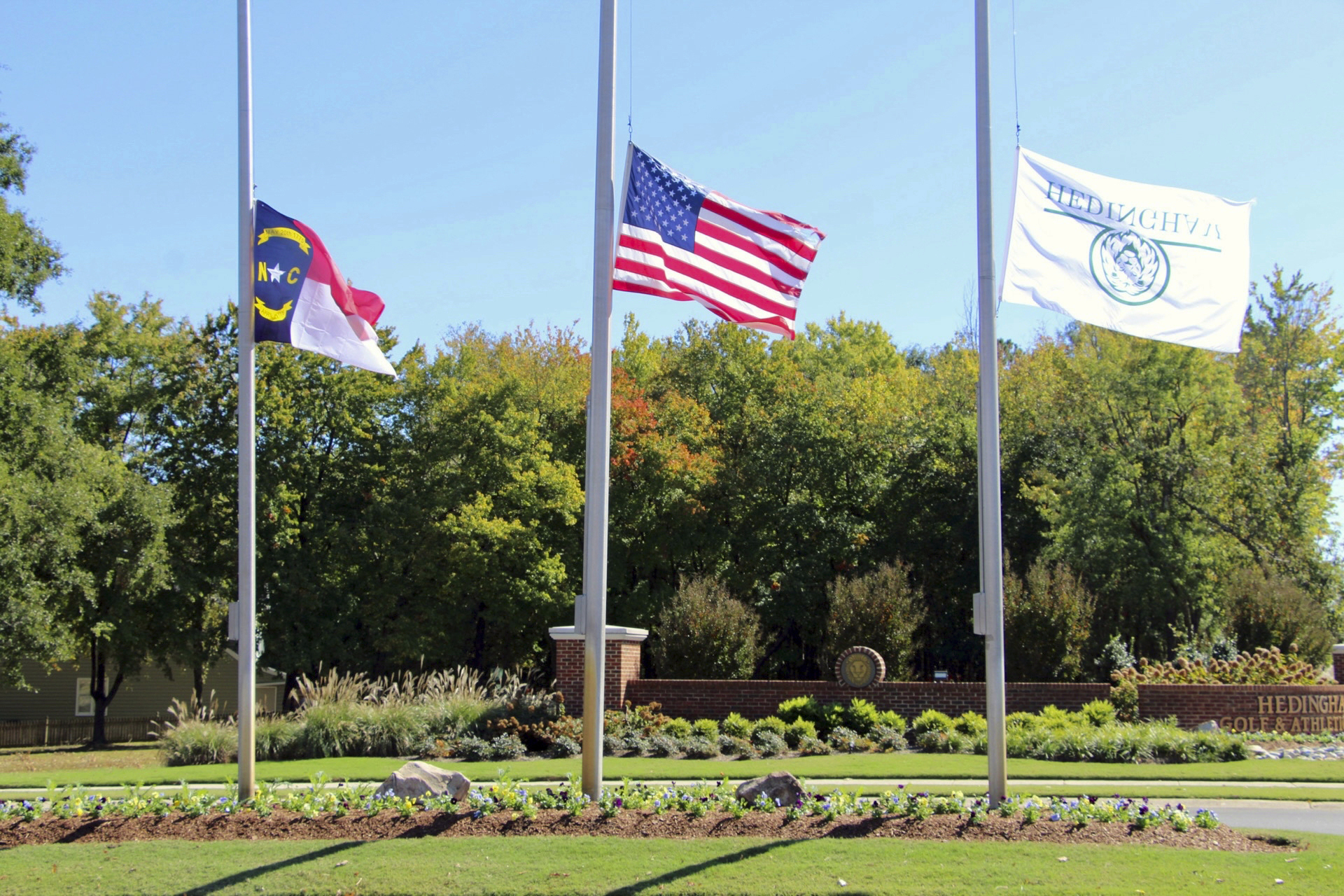 The North Carolina flag, American flag and Hedingham flag all fly at half-staff at the entrance to the Hedingham Golf Club in Raleigh, N.C., on Friday after a shooting in the community left five dead Thursday night, including one off-duty police officer.