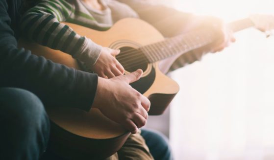 The above stock image is of a father teaching his son to play the guitar.