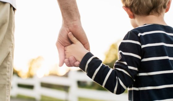 A father holds his son's hand in this stock image.