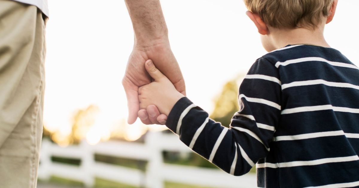 A father holds his son's hand in this stock image.